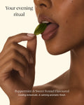 Close-up of a woman's hand and lower face holding a mint leaf near her lips, with text reading 'Your evening ritual' and 'Peppermint & Sweet Fennel Flavoured Cooling botanicals. A calming aromatic finish.