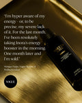 A black bottle of Inora Wake Up Call Energy drink supplement placed diagonally on a brushed gold metallic surface, with a customer testimonial quote and a black circular Vogue logo on the left side.